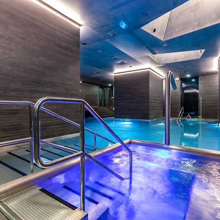 Grandhotel Pupp Karlovy Vary Luaran gambar The photo shows a modern spa area with a pool. There are sleek, dark walls and blue lighting that creates a tranquil atmosphere. A metal railing leads down into the pool, which has a section with bubbling water. The overall design features clean line