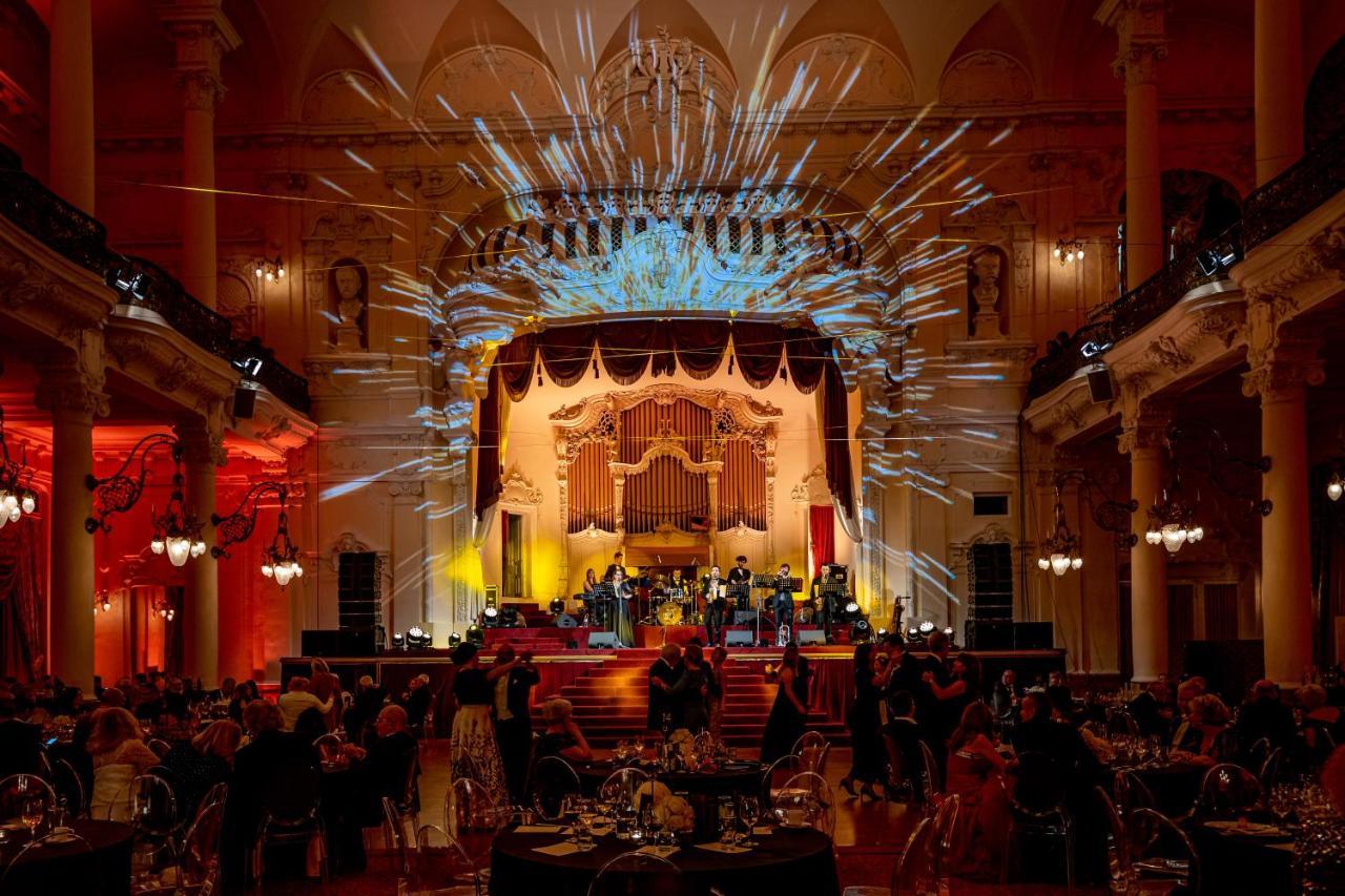 Grandhotel Pupp Karlovy Vary Luaran gambar The photo depicts an elegant event taking place in a grand hall. The stage is beautifully decorated with ornate details, featuring colorful lighting and dramatic spotlights. A band or ensemble is performing on stage, while guests are seated at elegan