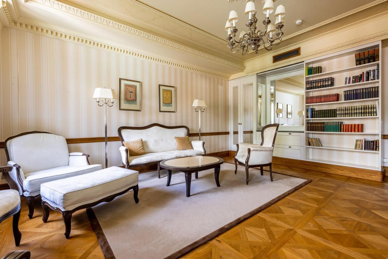 Grandhotel Pupp Karlovy Vary Luaran gambar The photo shows a spacious and elegantly designed living room. It features a light color palette with subtle striped wallpaper. In the center, there is a round coffee table surrounded by two armchairs and a modest sofa, all in a classic style. A chan