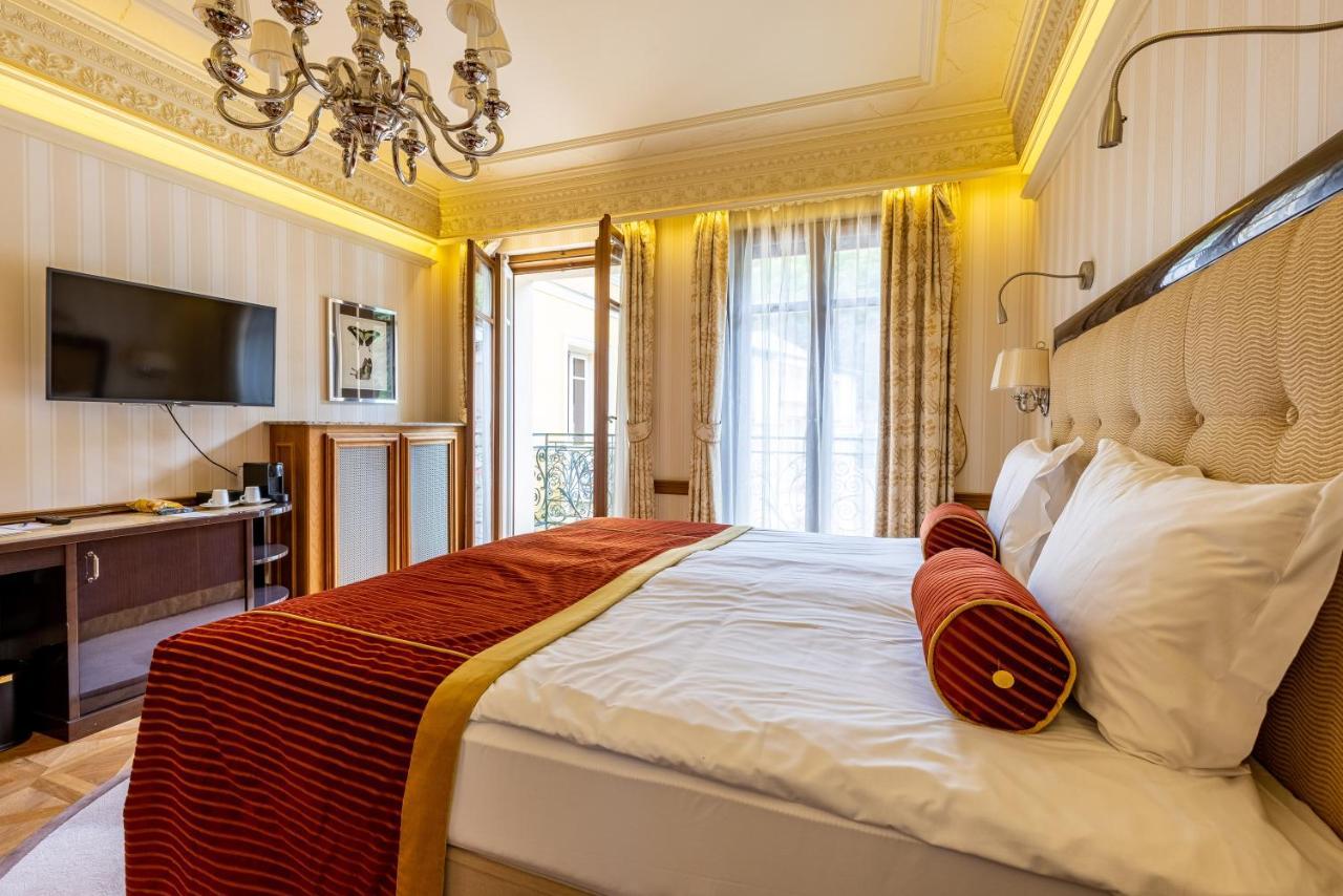 Grandhotel Pupp Karlovy Vary Luaran gambar The photo shows an elegant bedroom designed with a warm and inviting ambiance. There is a large bed dressed in white linens and accented with a rich red bedspread. Two decorative pillows are placed at the head of the bed, adding to the room's sophist