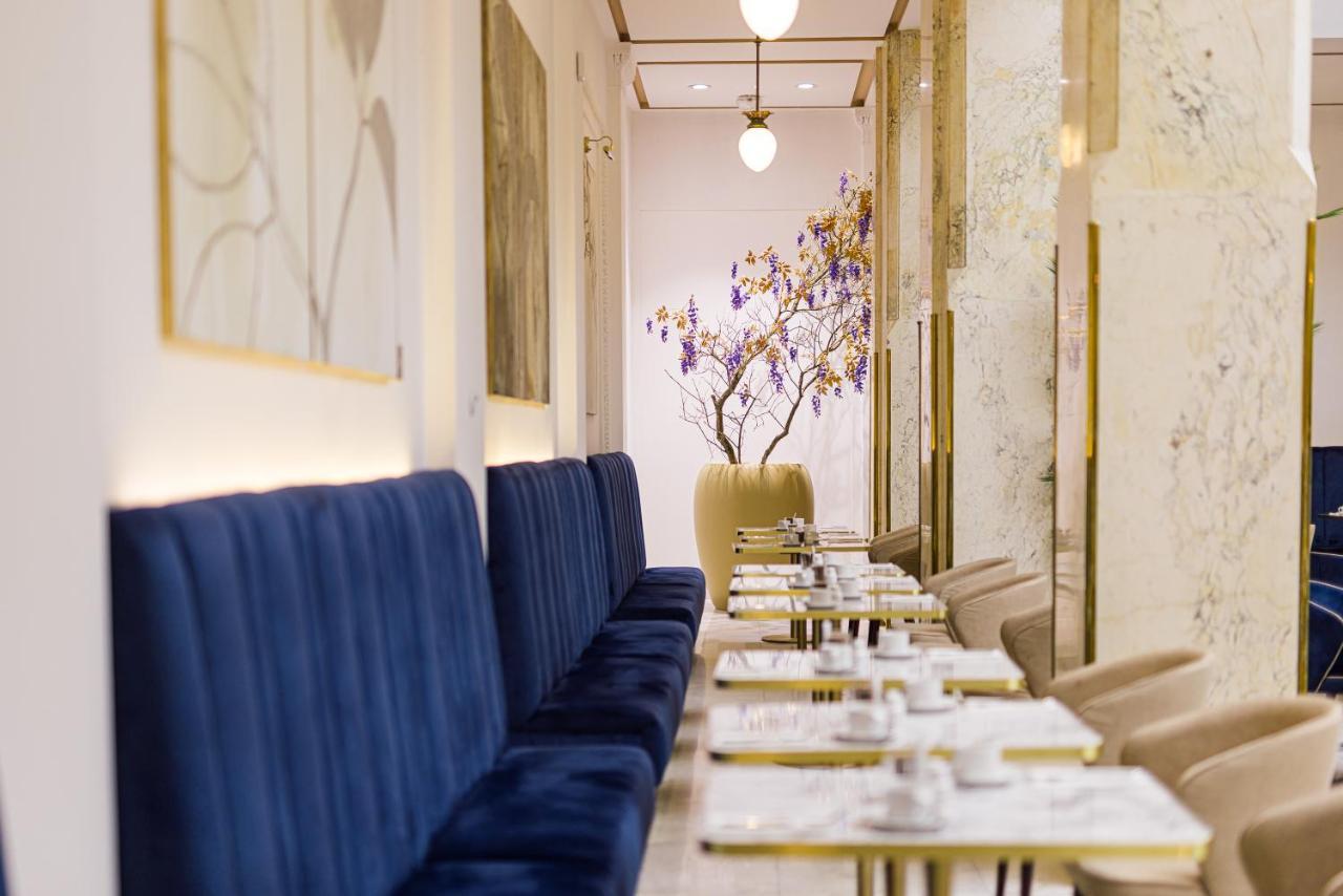 Grandhotel Pupp Karlovy Vary Luaran gambar The photo shows a stylish and elegant interior of a café or restaurant. On one side, there are long, plush blue benches against the walls, providing seating for guests. The tables are set with white plates and cutlery, suggesting a careful arrangemen