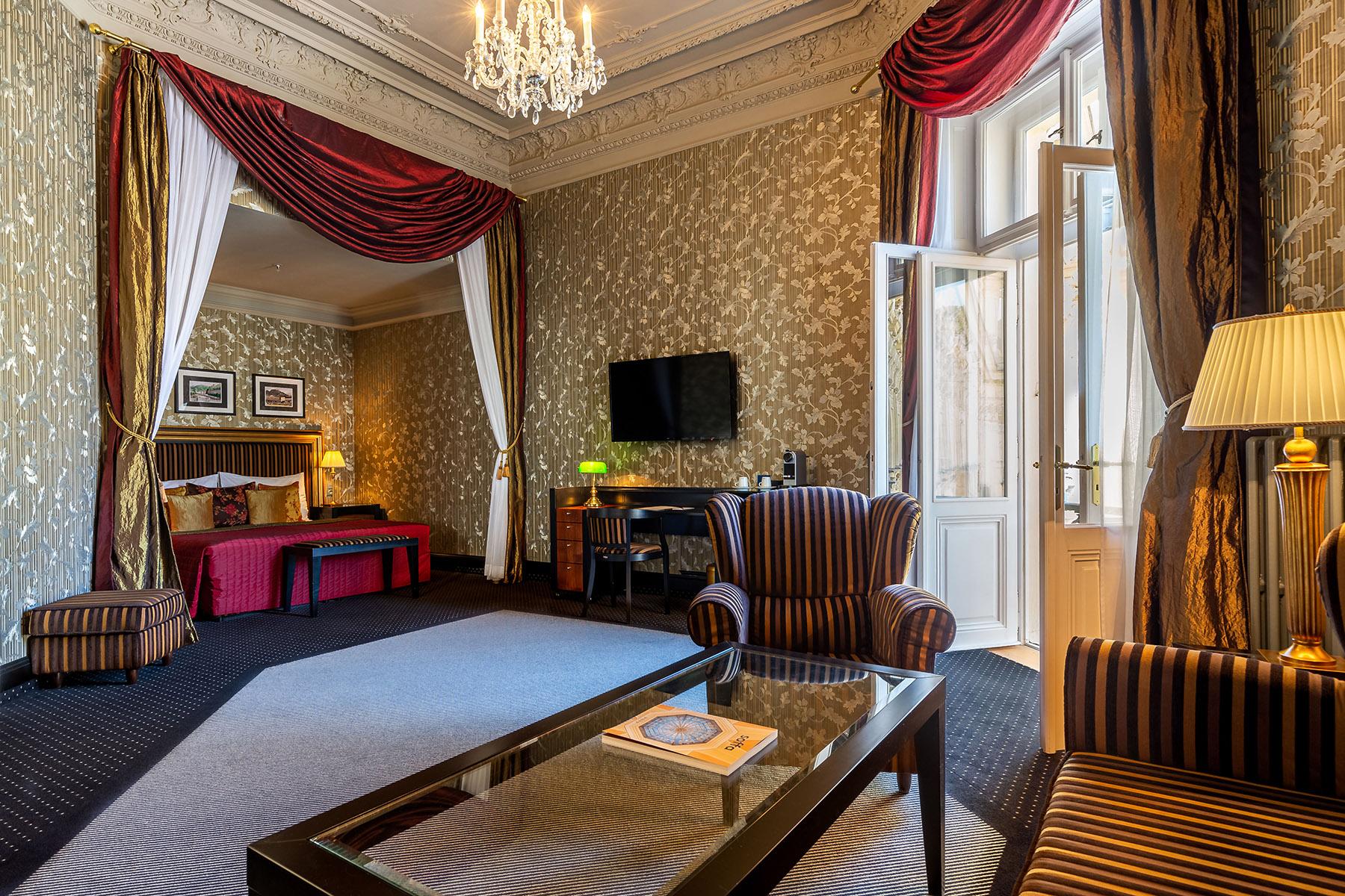 Grandhotel Pupp Karlovy Vary Luaran gambar The photo shows a luxurious hotel room featuring elegant decor. The room has tall windows with flowing curtains, a plush carpet, and ornate wallpaper. There are two comfortable armchairs with a stylish design positioned around a glass coffee table. A