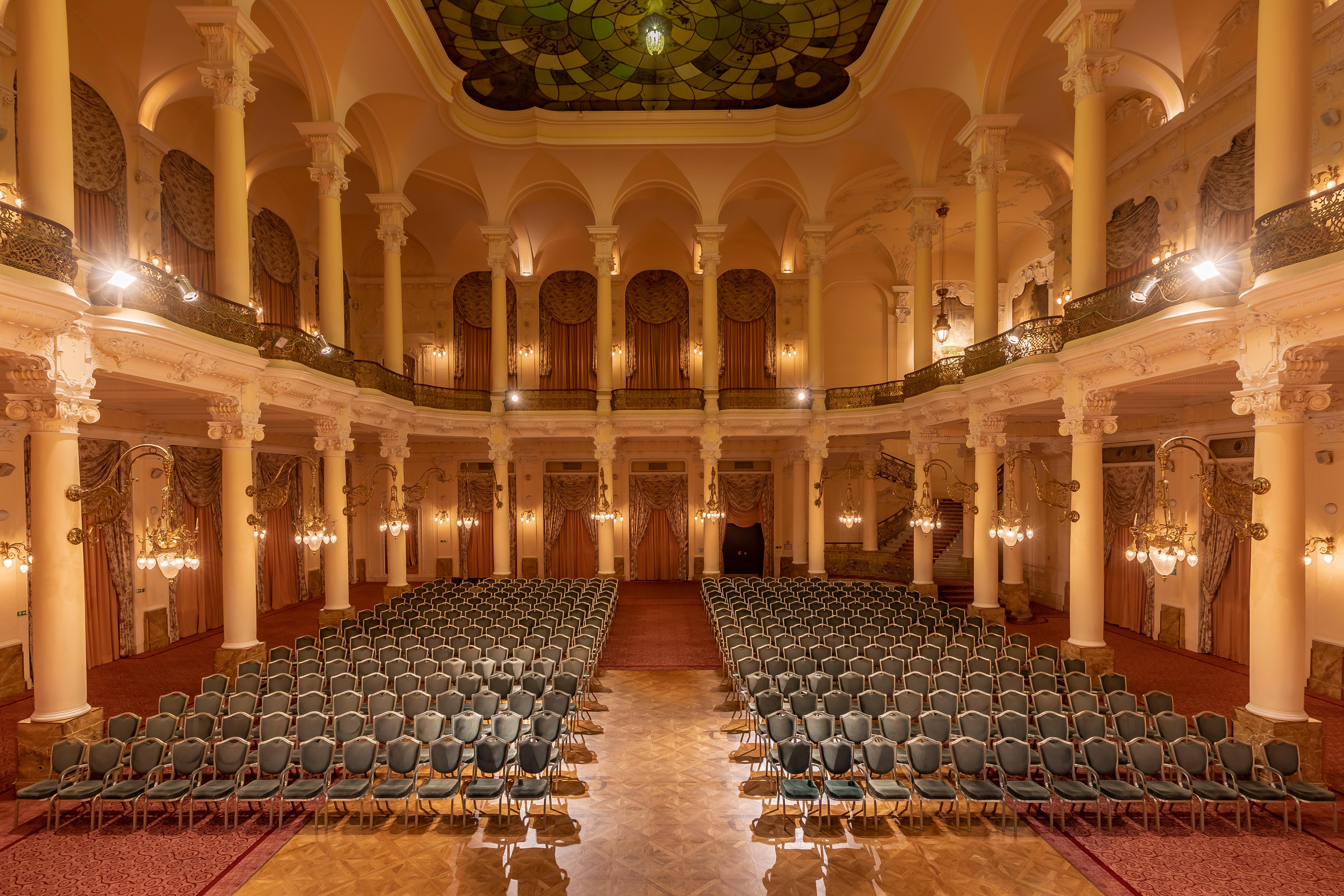 Grandhotel Pupp Karlovy Vary Luaran gambar The photo shows an elegant, spacious auditorium or hall, designed for events or performances. The interior features high ceilings supported by tall, decorative columns. Rows of green upholstered chairs are neatly arranged, suggesting the space is set