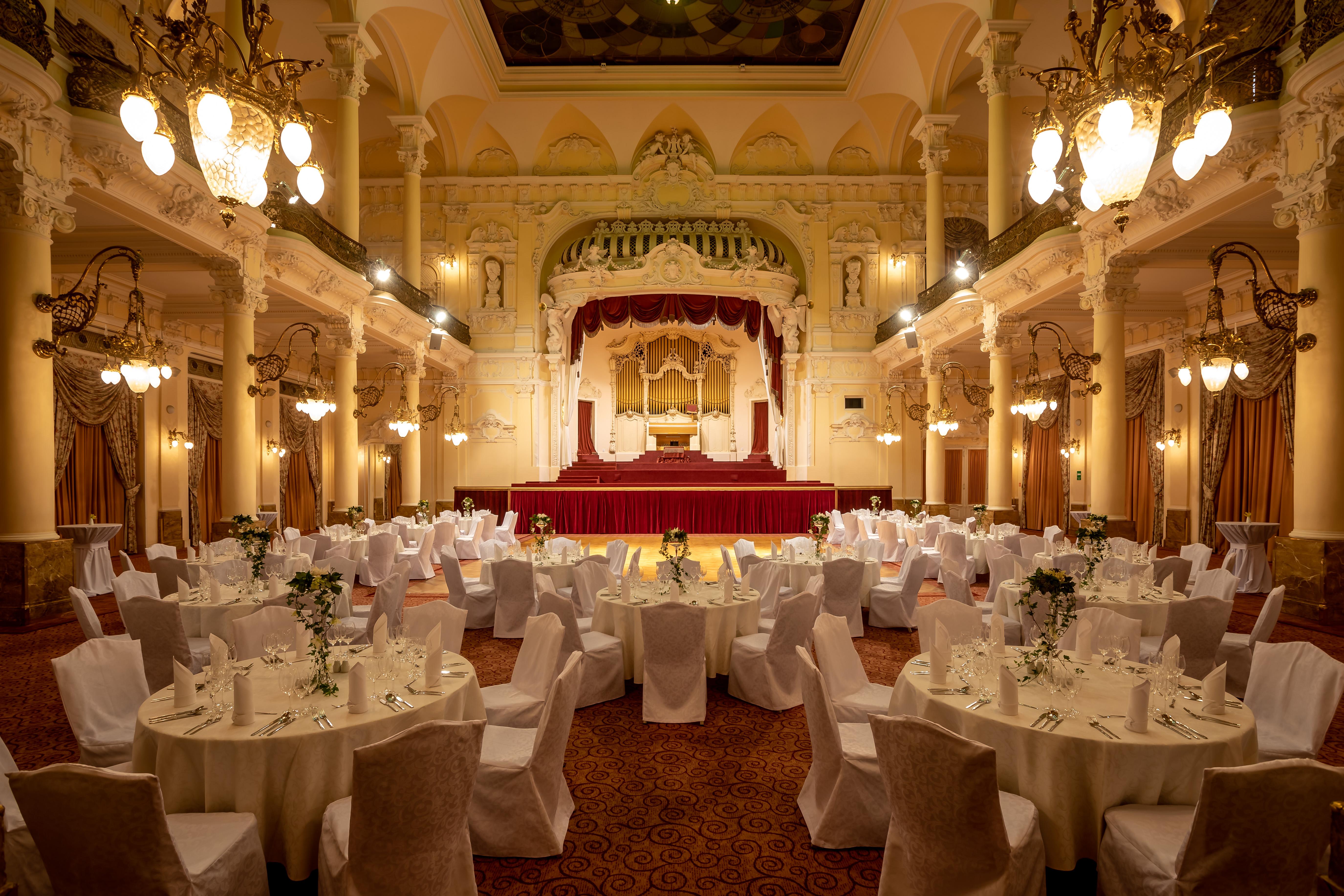 Grandhotel Pupp Karlovy Vary Luaran gambar The photo depicts an elegantly decorated banquet hall. The room features several round tables, each covered with white tablecloths and adorned with floral arrangements. Surrounding the tables are chairs, also draped in white fabric. 

The venue is ch