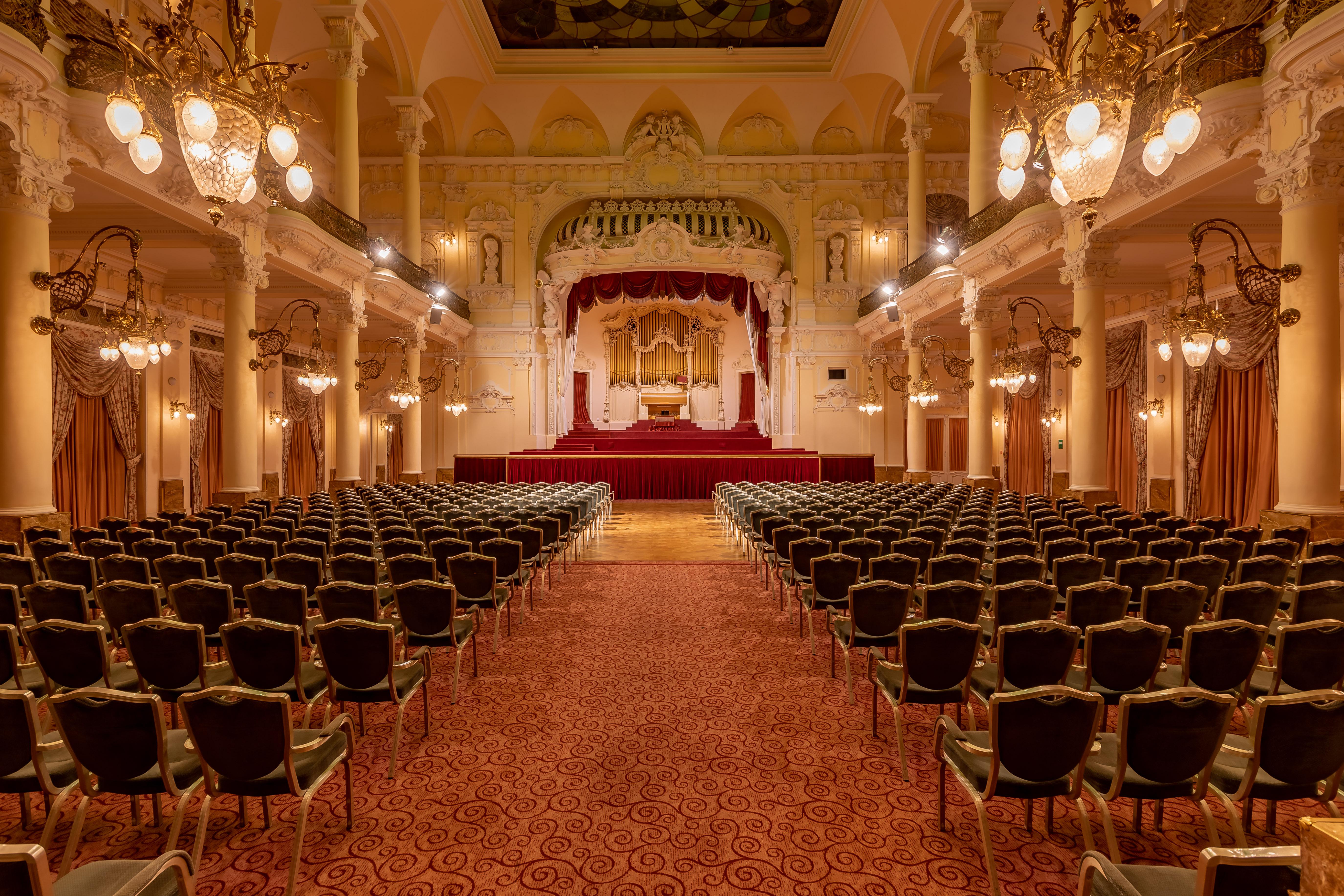 Grandhotel Pupp Karlovy Vary Luaran gambar The photo showcases an elegant interior of a theater or concert hall. It features a grand stage in the background, adorned with red curtains and decorative elements. The seating area is filled with rows of green upholstered chairs arranged in a symme