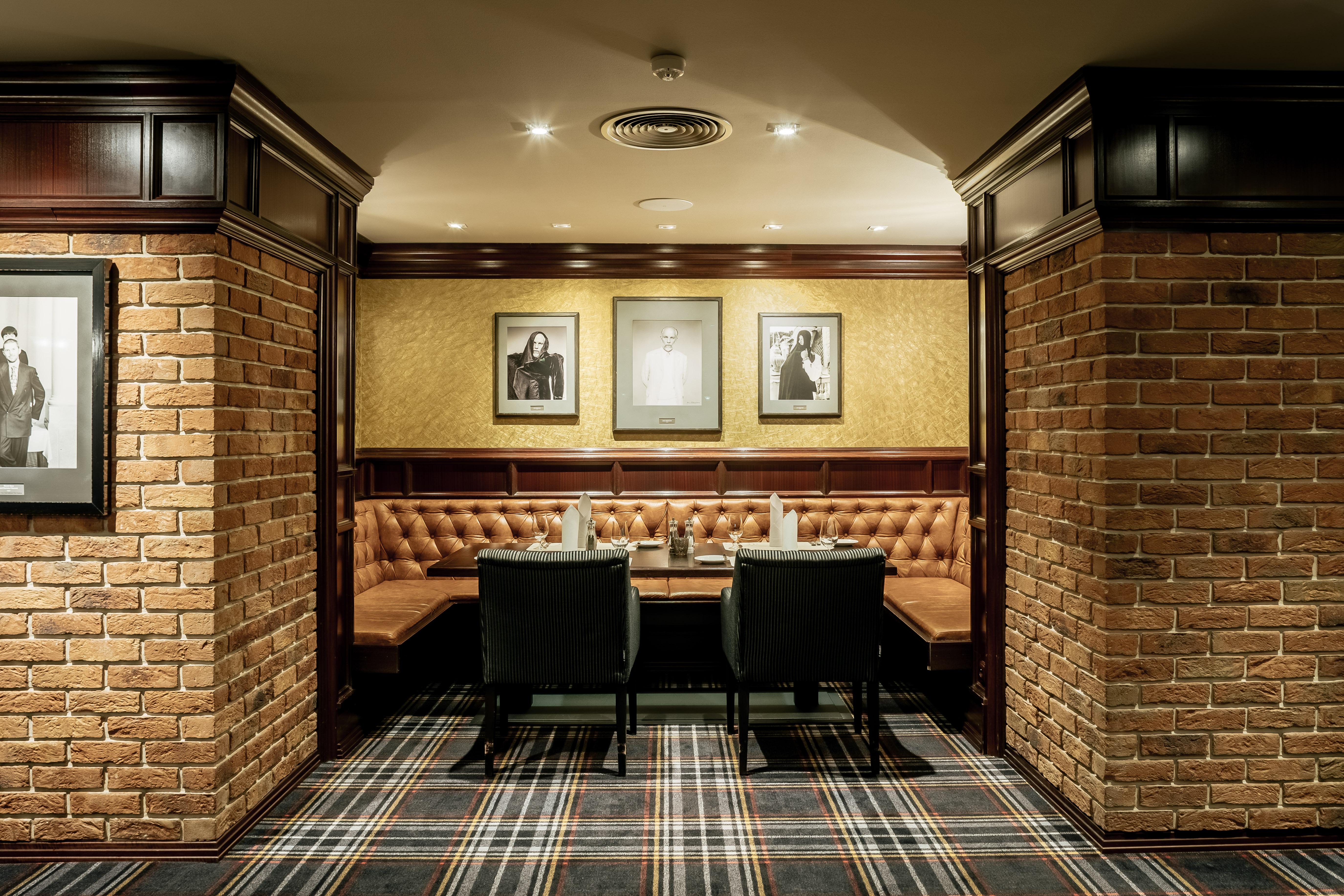 Grandhotel Pupp Karlovy Vary Luaran gambar The photo depicts a cozy interior of a room, likely a restaurant or lounge. It features brick walls, giving it a rustic feel, and wooden paneling adds a touch of elegance. There are two black chairs positioned at a wooden table. The seating area is c