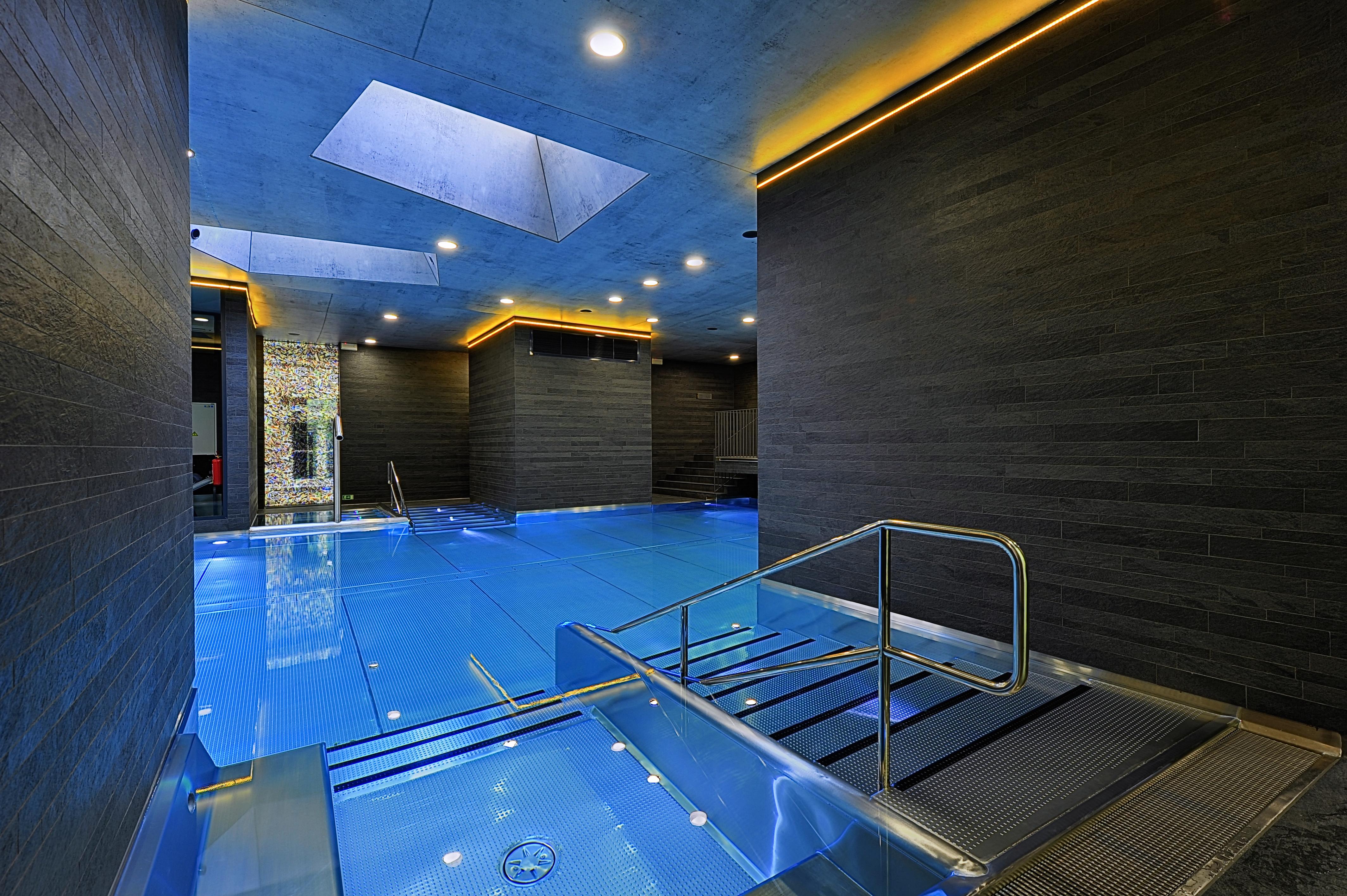 Grandhotel Pupp Karlovy Vary Luaran gambar The photo features a modern indoor swimming pool area. The pool is designed with a sleek, contemporary aesthetic, featuring a vibrant blue water surface. The surrounding walls are made of dark materials, possibly stone or wood, complemented by warm l