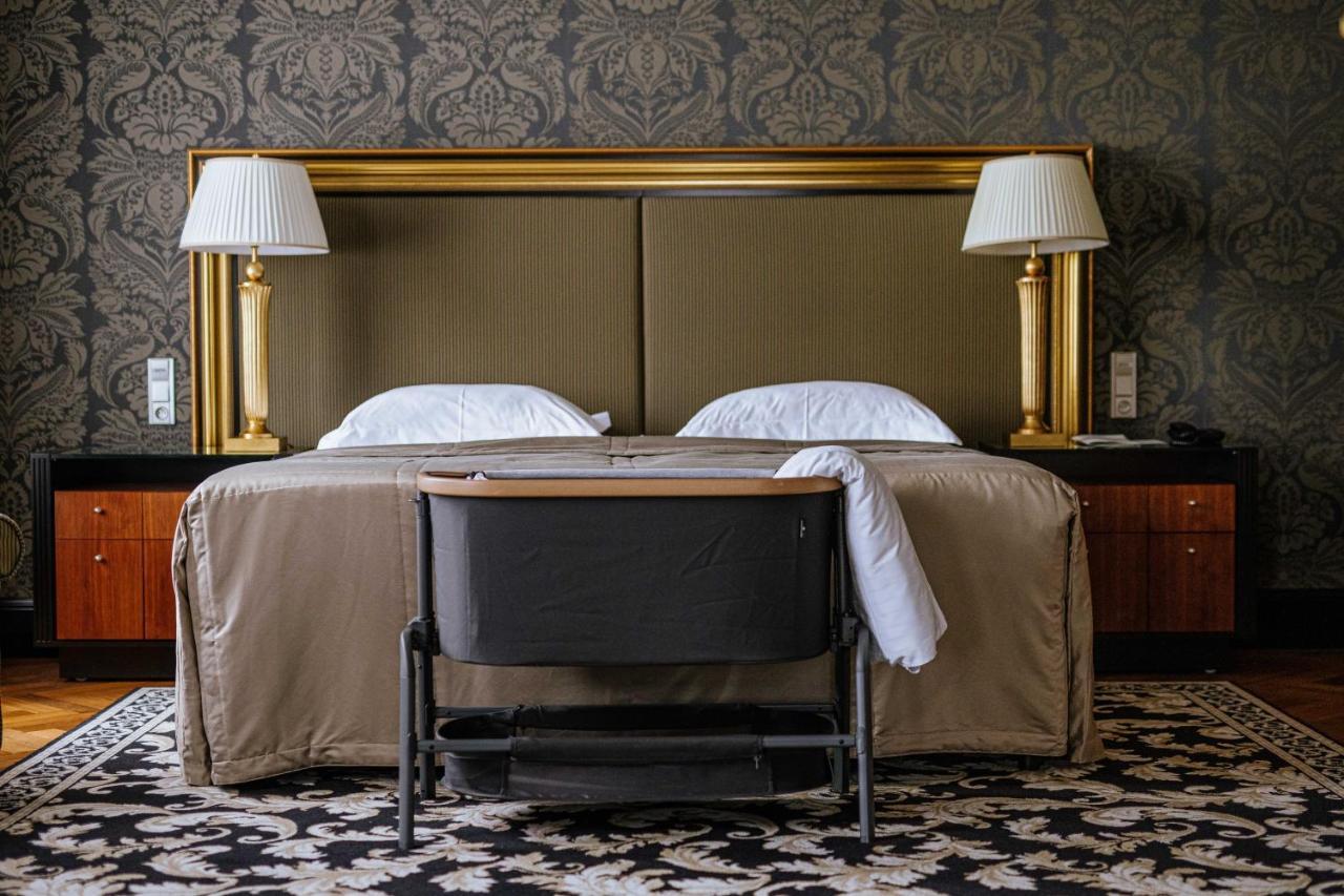 Grandhotel Pupp Karlovy Vary Luaran gambar The photo shows a cozy hotel room with a stylish design. In the center, there are two beds with white pillows and a beige bedspread. Flanking the beds are two elegant lamps on side tables, and behind the beds is a large gold-framed headboard. At the 