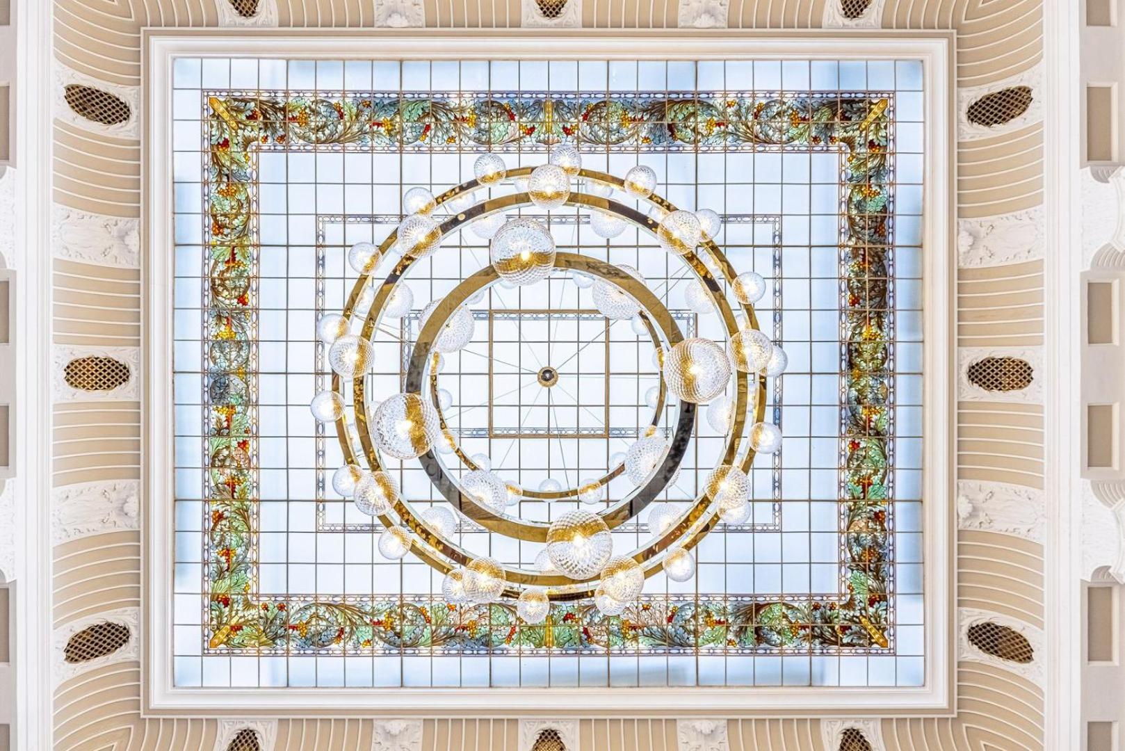 Grandhotel Pupp Karlovy Vary Luaran gambar The photo depicts an ornate ceiling design featuring a central circular lighting fixture surrounded by a decorative frame. The frame is embellished with intricate patterns and colors, possibly including floral or geometric motifs. The outer edges sho